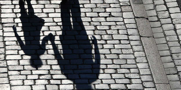 Die Schatten eines Erwachsenen und eines Kindes sind auf einem Kopfsteinpflaster zu sehen