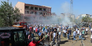 Menschen stehen vor einem teilweise zerstörten Gebäude und rauchenden Trümmern