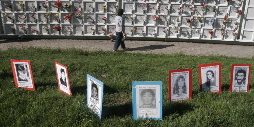 eine Wand mit Urnengräbern, davor Pappschilder mit Porträtaunahmen