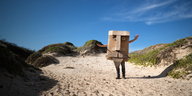 Ein Mensch mit Pappkartonverkleidung steht am Strand