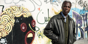Der Fotograf Akinbode Akinbiyi vor einer Mauer, die mit Graffiti besprüht ist