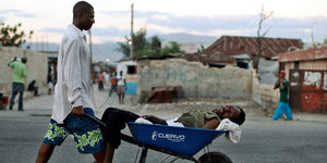 Ein Mann transportiert einen Kranken in einer Schubkarre