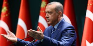 Erdogan mit nach oben gerichteten Handflächen vor türkischen Fahnen