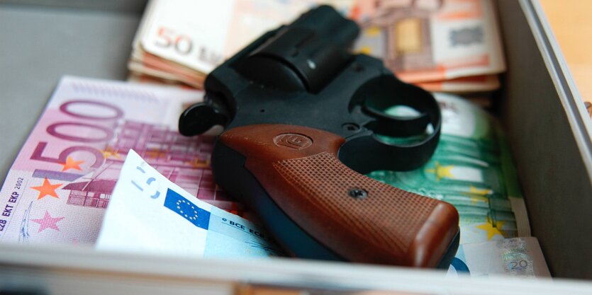 In einer Kasse liegt auf den Geldscheinen ein Revolver