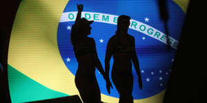 Zwei Beachvolleyballerinnen im Schatten, im Hintergrund die brasilianische Fahne