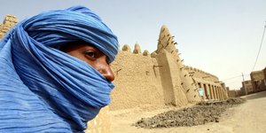 Ein Tuareg-Mann mit blauem Schleier steht vor einem der Mausoleen von Timbuktu