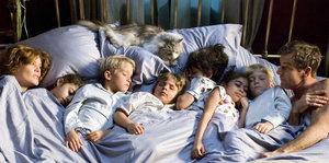 Eine Frau, ein Mann und sechs Kinder schlafen in einem Bett