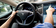 Ein Mann sitzt in einem Auto von Tesla und zeigt auf einen Bildschirm