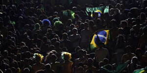 Sportfans im dunkeln, ein paar von ihnen tragen bunte Perücken und Brasilienfahnen
