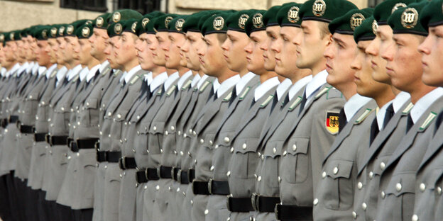 Rekruten in Uniformen und mit Baretten stehen in einer Reihe