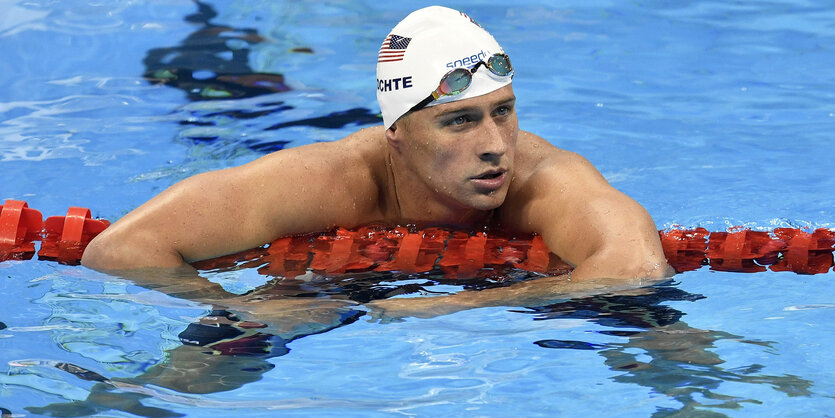 Ryan Lochte mit Badekappe im Wasser, die Arme auf der Bahnabsperrung