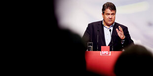 SPD-Chef Sigmar Gabriel steht hinter einem roten Rednerpult, redet und gestikluiert dabei mit der linken Hand. Im Vordergrund sind unscharf Zuhörer zu erkennen