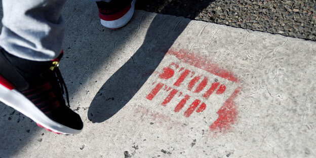 Ein Turnschuh läuft neben dem Graffito “Stop TTIP“ her