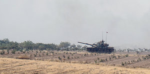 Ein Panzer fährt an einem staubigen Feld vorbei