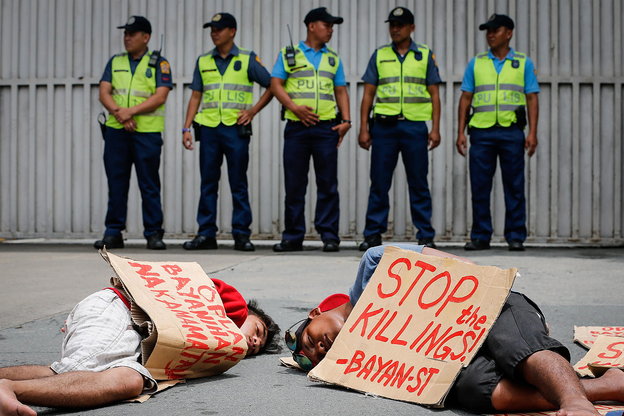 Zwei Männer liegen mit Plakaten vor einer Reihe von Polizisten