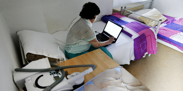 Eine Frau sitzt auf einem Bett an einem Laptop Eine Frau sitzt auf einem Bett an einem Laptop
