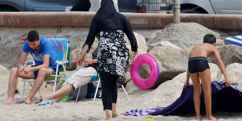 Eine Frau trägt ein langes Hemd und ein Kopftuch an einem Strand