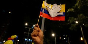 Ein Fähnchen Kolumbiens mit einer Friedenstaube bei einer nächtlichen Kundgebung