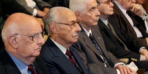 Ältere Männer sitzen nebeneinander, sie tragen Anzug und Krawatte