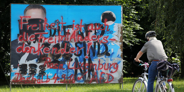 Ein Radfahrer vor einem durchgekritzeltem Poster der AfD