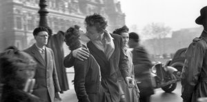 Ein schwarz-weiß Bild, eine Szene aus dem Jahr 1950: Ein junges Paar küsst sich inmitten von vorbeigehenden Menschen.