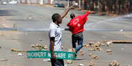 Ein Mann hält ein Schild mit der Aufschrift "Robert Mugabe Rd" und zeigt in die Ferne