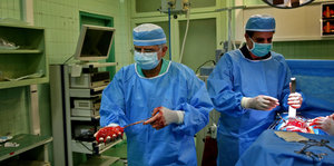 Ein Arzt in blauem Kittel trägt eine Niere durch ein Krankenhauszimmer