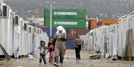 Eine Frau und mehrere Kinder laufen zwischen Reihen weißer Container entlang