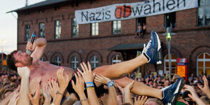 Ein Mann, der in ein MIcrophon spricht, wird auf Händen getragen, dahinter ein Transparent „Nazis abwählen“