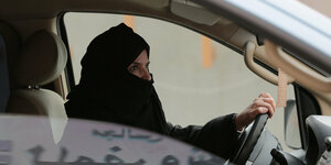 Eine Frau trägt einen Schleier und sitzt am Auto