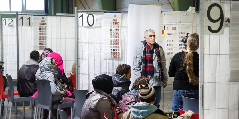 Menschen stehen und sitzen an numerierten Ständen mit Trennwänden