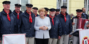Angela Merkel steht zwischen den Mitglieder eines Fischerchores