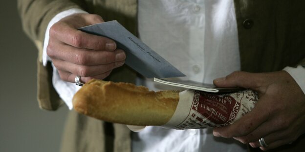Ein Mensch hält ein Baguette und ein Papier in den Händen