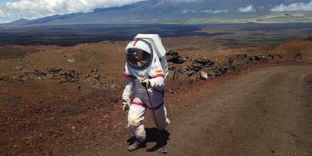 Eine Frau läuft im Astronautinnenanzug in einer bergigen Landschaft