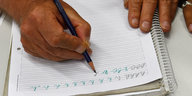 Eine Hand hält einen Stift und schreibt damit mehrfach den Buchstaben „h" auf ein Blatt Papier