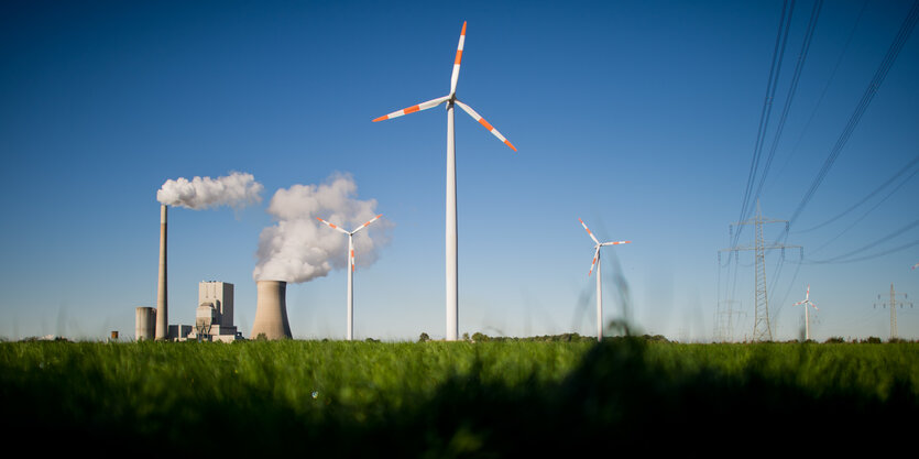 Auf einer Wiese steht ein Windrad neben einem Kohlekraftwerk im Hintergrund