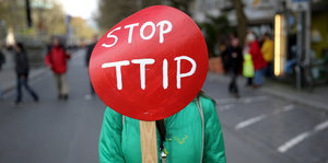 Eine Frau hält ein rotes Schild, auf dem „Stop TTIP“ steht