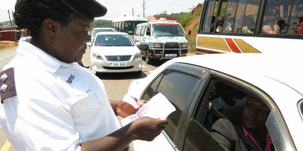 Eine Polizistin steht neben einem Auto und hat Papiere in der Hand