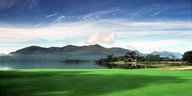Eine Landschaft in Irland: grüne Wiese, eine See und im Hintergründ dunkle Berge