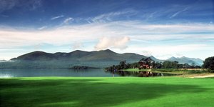 Eine Landschaft in Irland: grüne Wiese, eine See und im Hintergründ dunkle Berge