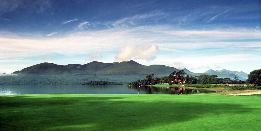 Eine Landschaft in Irland: grüne Wiese, eine See und im Hintergründ dunkle Berge