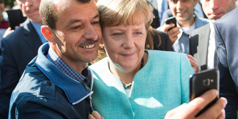 Ein Mann macht ein Selfie von sich und einer Frau in hellblauem Anzug