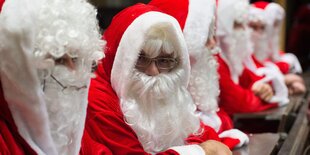 Mehrere Menschen, die als Weihnachtsmänner verkleidet sind, sitzen nebeneinander