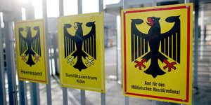 drei Schilder mit dem Bundesadler an einem Tor, auf dem vorderen steht „Amt für den Militärischen Abschirmdienst“