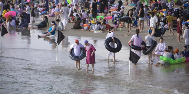 Menschen in Badebekleidung stehen am Strand im Wasser