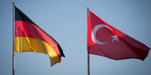 eine deutsche und eine türkische Nationalflagge wehen im Wind vor blauem Himmel