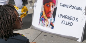 Auf einem Plakat steht: Caine Rogers, unbewaffnet und getötet