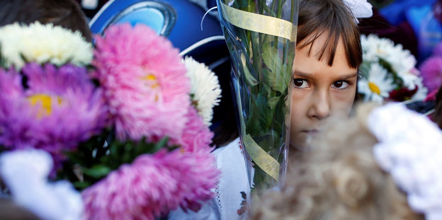 Ein ukrainisches Schulmädchen versteckt sich hinter einem Strauß Blumen, den sie zum Schulanfang erhalten hat