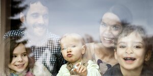 Eine Familie mit drei Kindern und zwei Eltern lächeln in die Kamera