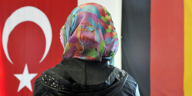 Frau mit buntem Kopftuch von hinten, vor einer türkischen Fahne